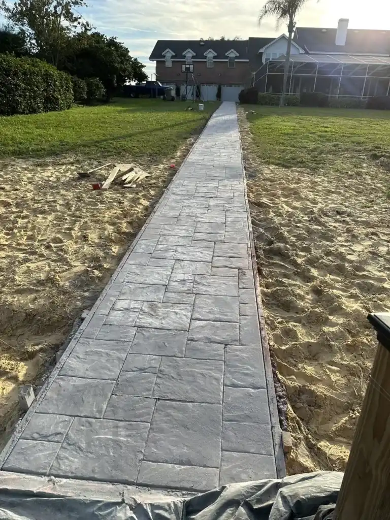 Gray stamped concrete walkway across a sandy yard toward a house, Heritage Pines, FL